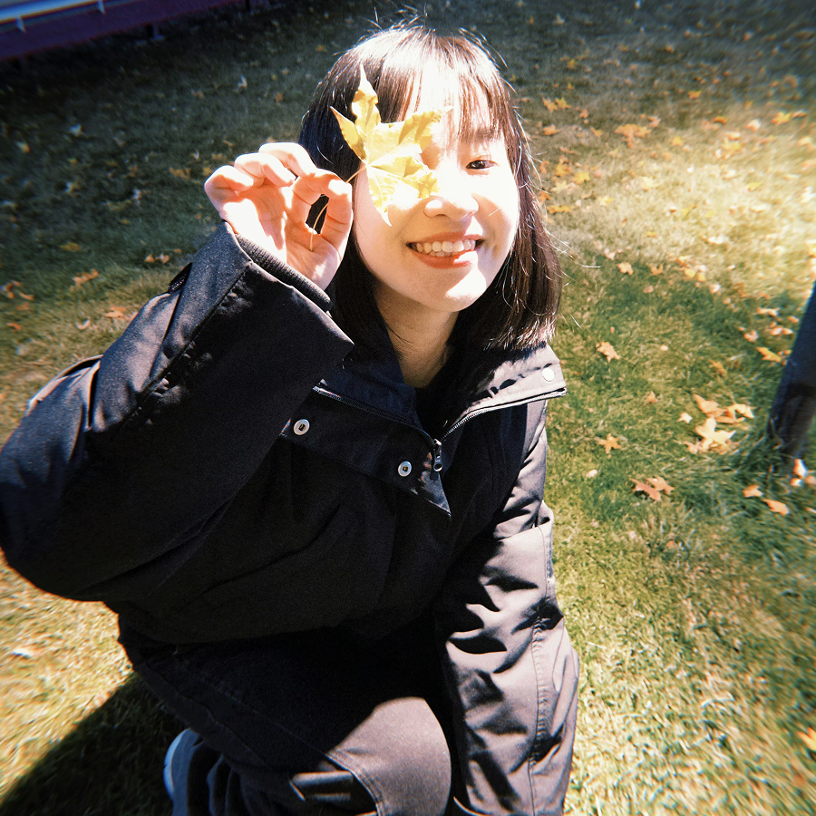 杜舒惠在户外，拿着一片黄色树叶微笑